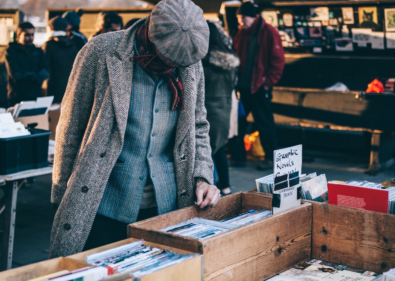 services-01 A man in vintage clothing browses through books at an outdoor market.
